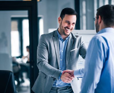 two-smiling-businessmen-shaking-hands-while-standing-in-an-office (1)-min